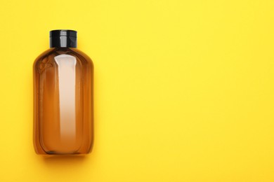 Bottle of shampoo on yellow background, top view. Space for text
