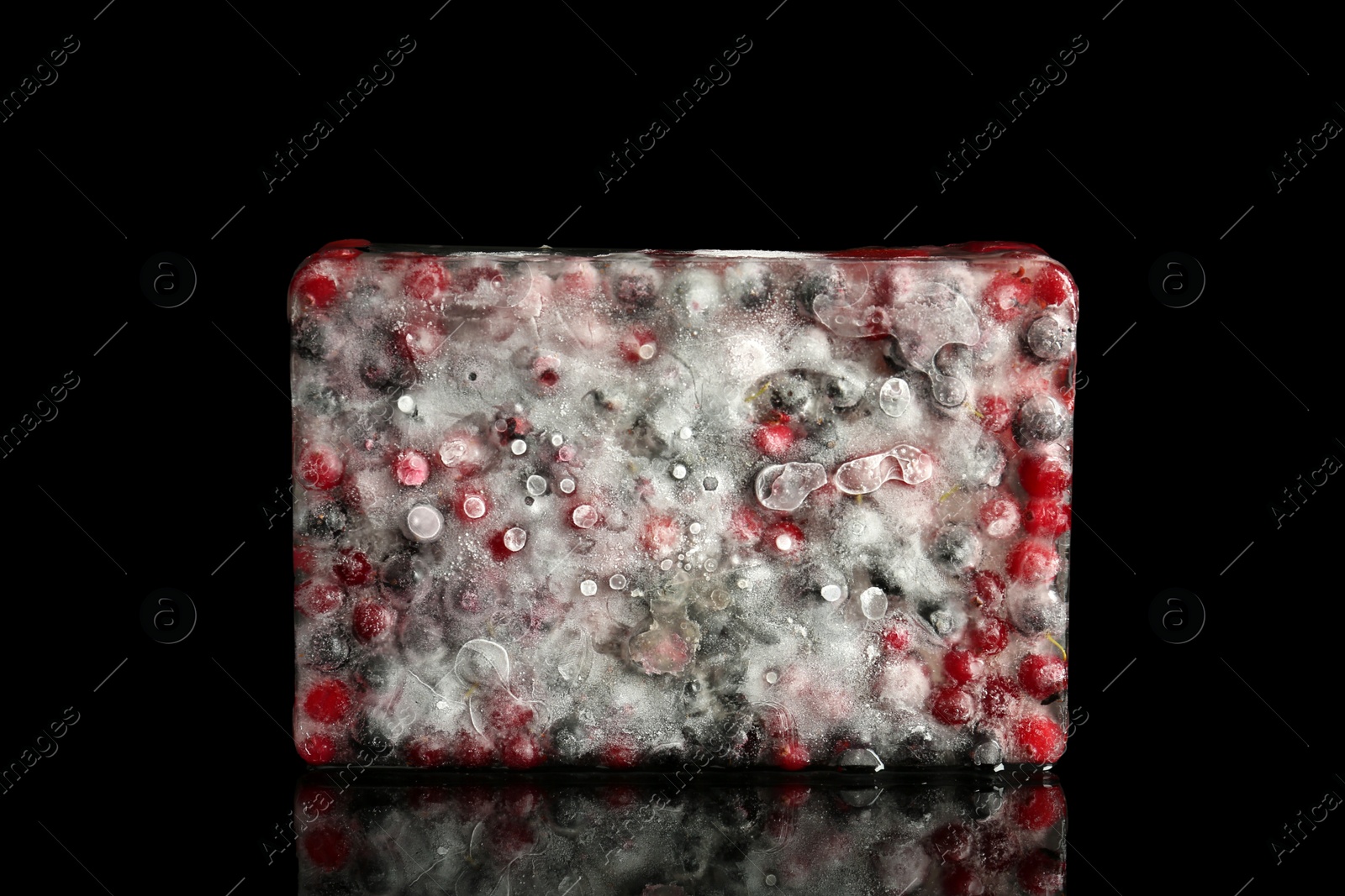 Photo of Fresh berries frozen in ice cube on dark table