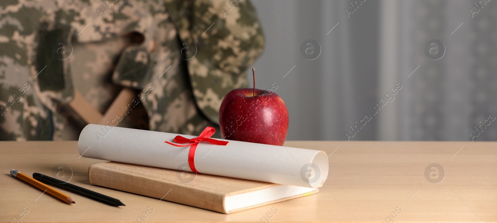 Image of Military education. Diploma, apple and stationery on wooden table, space for text. Chair with soldier's jacket indoors
