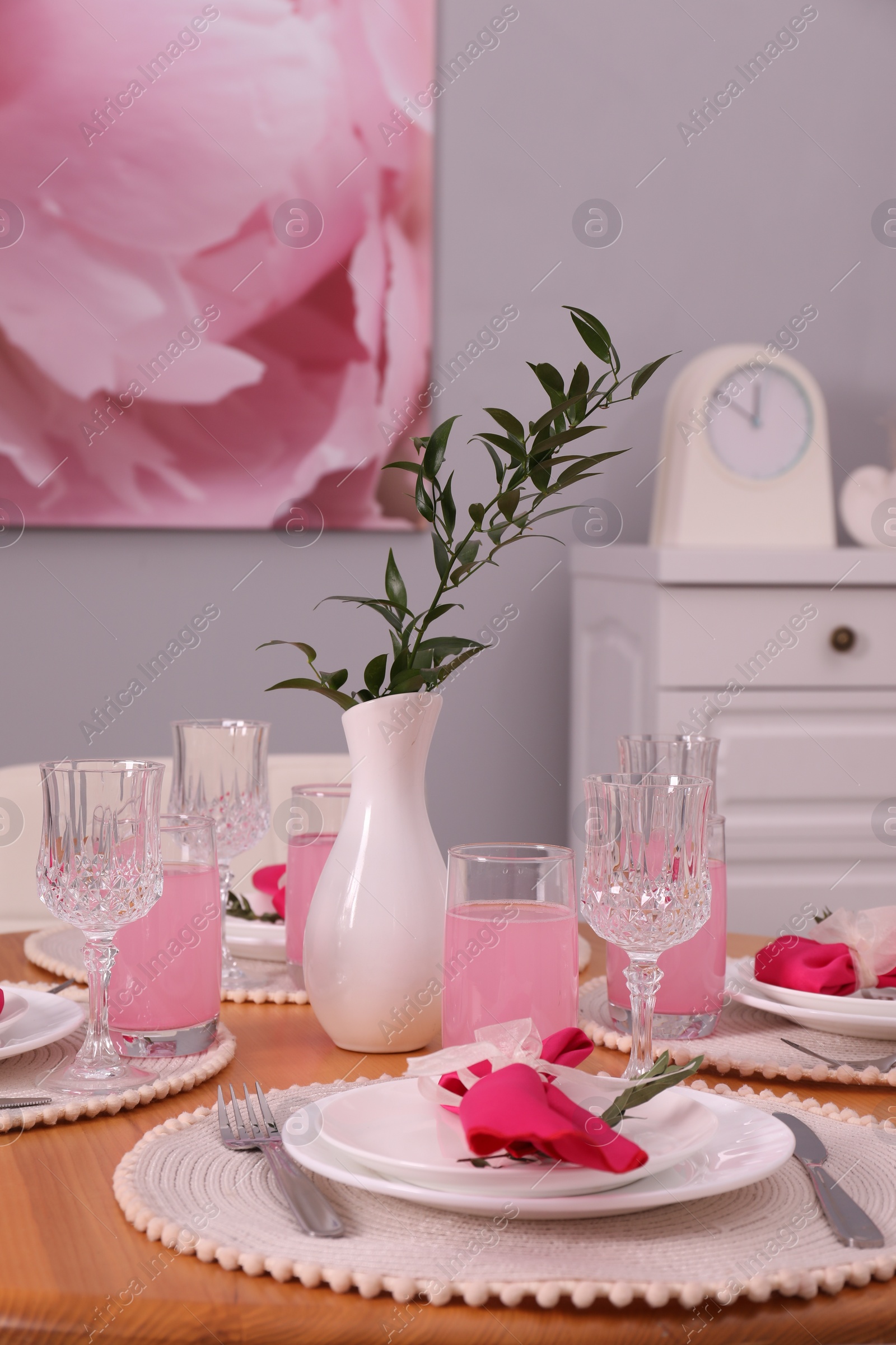 Photo of Color accent table setting. Glasses, plates, vase with green branch and pink napkins in dining room