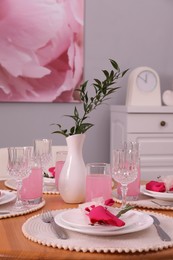 Photo of Color accent table setting. Glasses, plates, vase with green branch and pink napkins in dining room