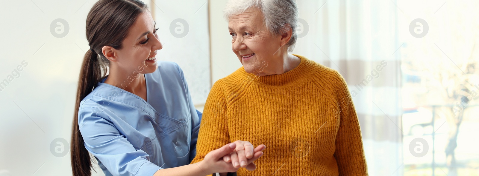 Image of Care worker helping elderly woman to walk in geriatric hospice. Banner design