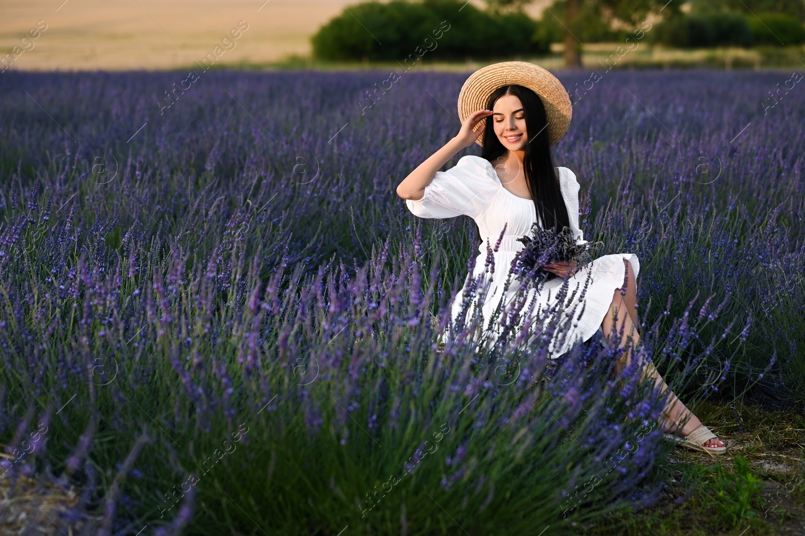 Photo of Beautiful young woman with bouquet sitting in lavender field