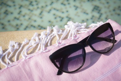 Photo of Stylish sunglasses and blanket near outdoor pool on sunny day, closeup. Space for text