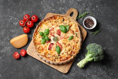 Tasty quiche with tomatoes, basil and cheese served on dark textured table, flat lay