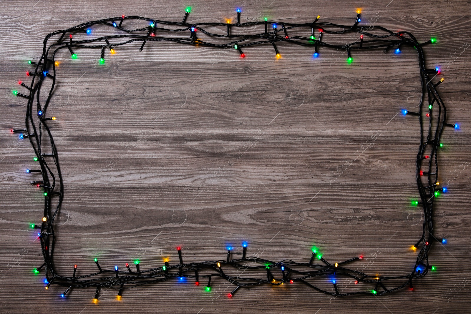 Photo of Frame of Christmas lights on wooden table, top view. Space for text