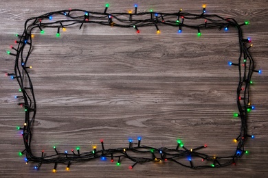 Photo of Frame of Christmas lights on wooden table, top view. Space for text