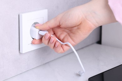 Photo of Woman plugging smartphone into power socket at white table indoors, closeup