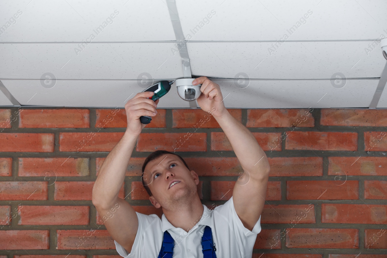 Photo of Technician installing CCTV camera on ceiling indoors