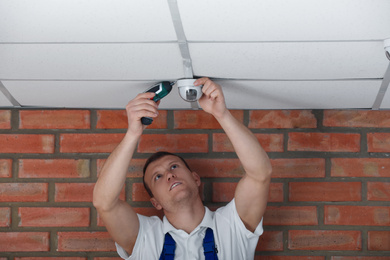 Photo of Technician installing CCTV camera on ceiling indoors