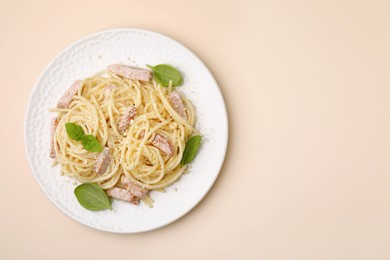 Photo of Plate of tasty pasta Carbonara with basil leaves on beige background, top view. Space for text