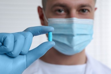 Doctor holding pill on light background, selective focus. Space for text