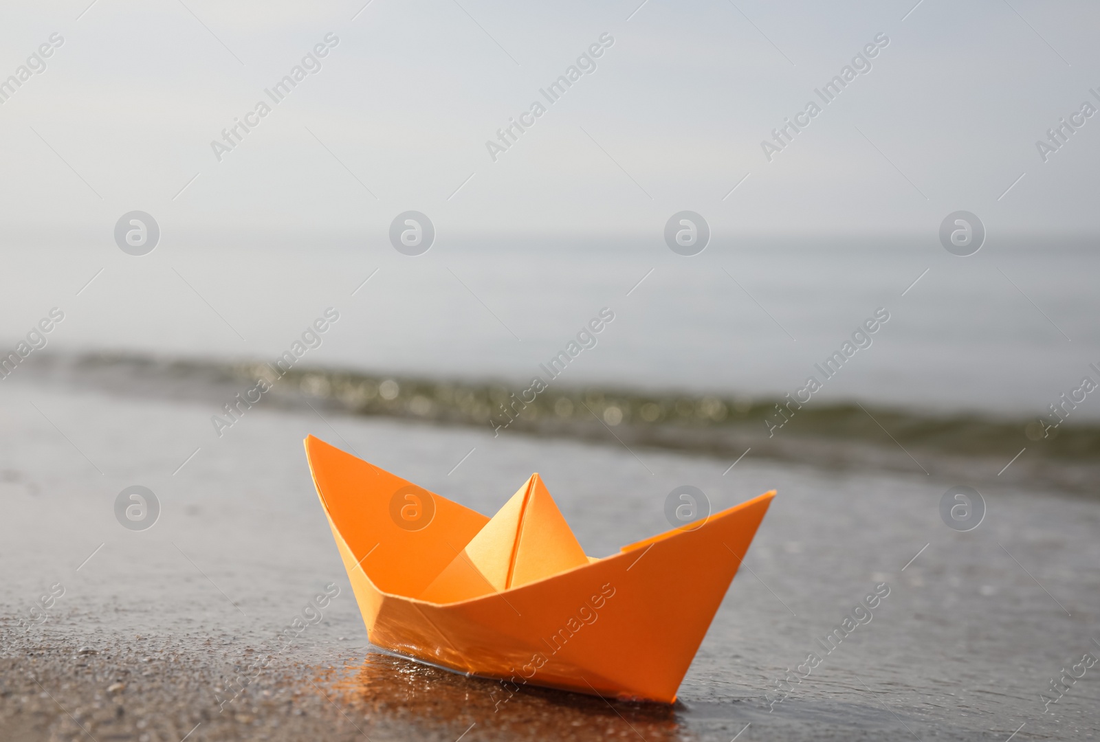 Photo of Orange paper boat on sandy beach near sea, space for text