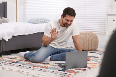 Photo of Happy man greeting someone during video chat via laptop at home