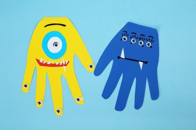 Photo of Funny hand shaped monsters on light blue background, flat lay. Halloween decoration