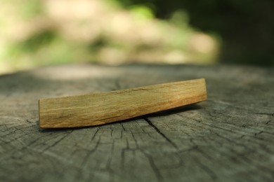 Photo of Palo santo stick on wooden stump outdoors, closeup