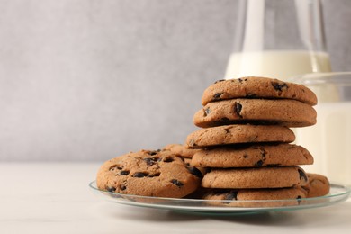 Photo of Delicious chocolate chip cookies and milk on white marble table. Space for text