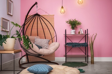 Photo of Cozy apartment with hanging chair near wall. Type of armchair for interior design