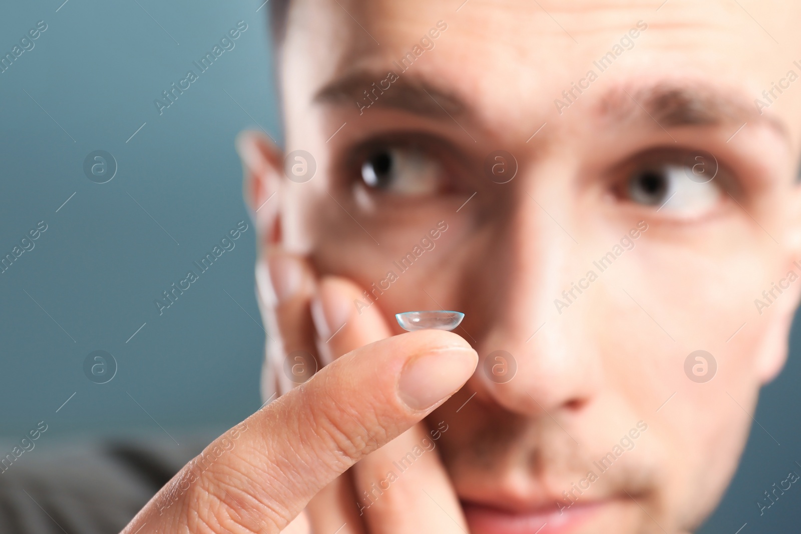 Photo of Young man putting contact lens in his eye on color background