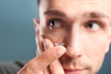 Photo of Young man putting contact lens in his eye on color background