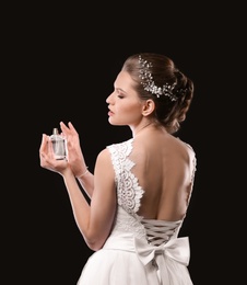 Photo of Beautiful young bride with bottle of perfume on black background