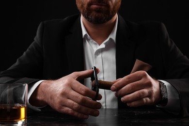 Photo of Man cutting tip of cigar at dark marble table, closeup