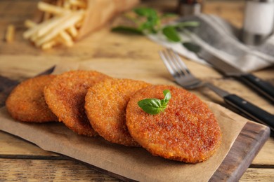Photo of Delicious fried breaded cutlets with basil on wooden table