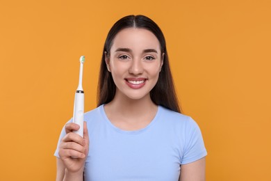 Photo of Happy young woman holding electric toothbrush on yellow background