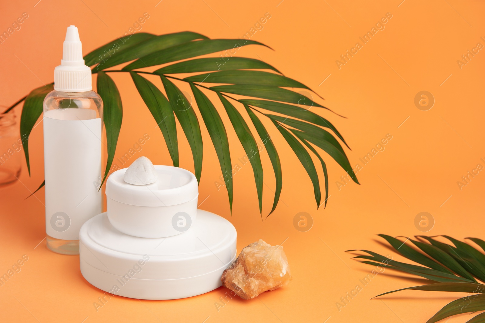 Photo of Cosmetic products, quartz gemstone and palm leaf on orange background