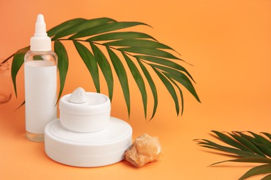 Photo of Cosmetic products, quartz gemstone and palm leaf on orange background