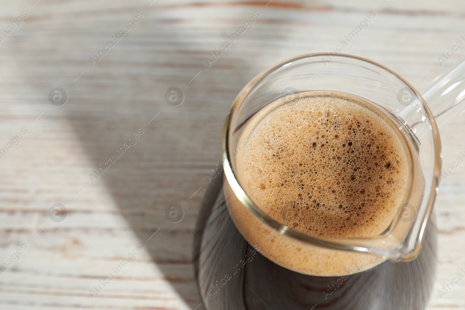 Photo of Glass turkish coffee pot with hot drink on wooden table, above view. Space for text