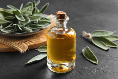 Photo of Bottle of essential sage oil and leaves on black table