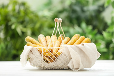 Photo of Raw yellow carrots in basket on white wooden table against blurred background