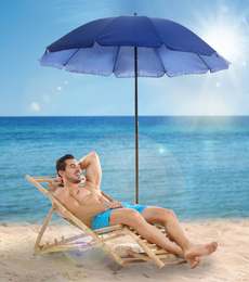 Image of Young man on lounger under umbrella for sun protection at sandy beach