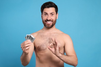 Photo of Naked man with condoms showing ok gesture on light blue background. Safe sex