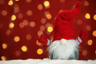 Photo of Cute Christmas gnome on snow against blurred festive lights. Space for text