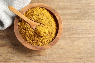 Photo of Dry curry powder in bowl and spoon on wooden table, top view. Space for text