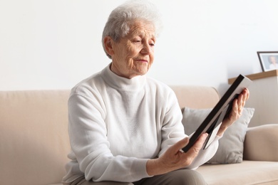 Elderly woman with framed photo on sofa at home