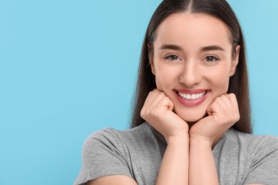 Photo of Young woman with clean teeth smiling on light blue background, space for text