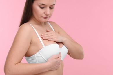 Photo of Mammology. Woman in bra doing breast self-examination on pink background