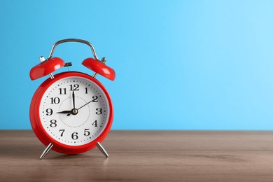 Photo of Red alarm clock on wooden table against light blue background, space for text