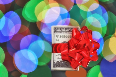 Photo of Dollar bills with gift bow against blurred lights, space for text. Bokeh effect
