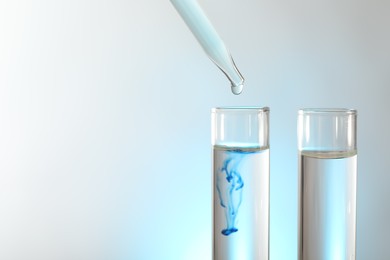 Photo of Dripping liquid from pipette into test tube on light background, closeup. Space for text