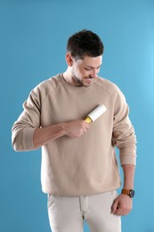 Photo of Man cleaning clothes with lint roller on light blue background