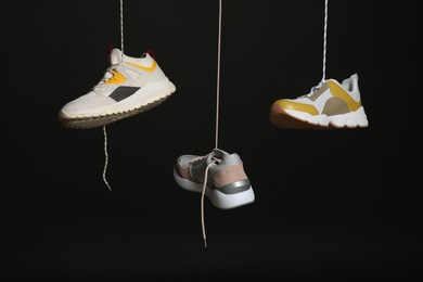 Photo of Different sneakers hanging on black background. Stylish shoes