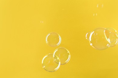 Photo of Beautiful transparent soap bubbles on yellow background