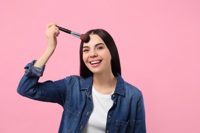 Photo of Smiling woman applying makeup with brush on pink background