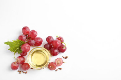 Organic red grapes, seeds and bowl of natural essential oil on white background, flat lay. Space for text