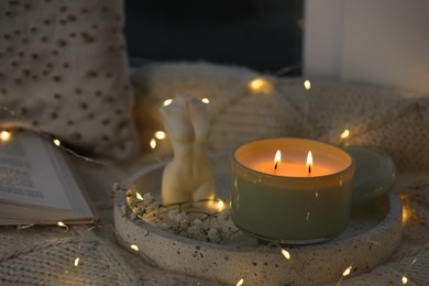 Photo of Tray with beautiful candles, fairy lights, book and knitted blanket on window sill
