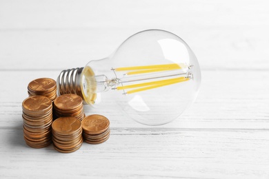 Photo of Light bulb and coins on white wooden background